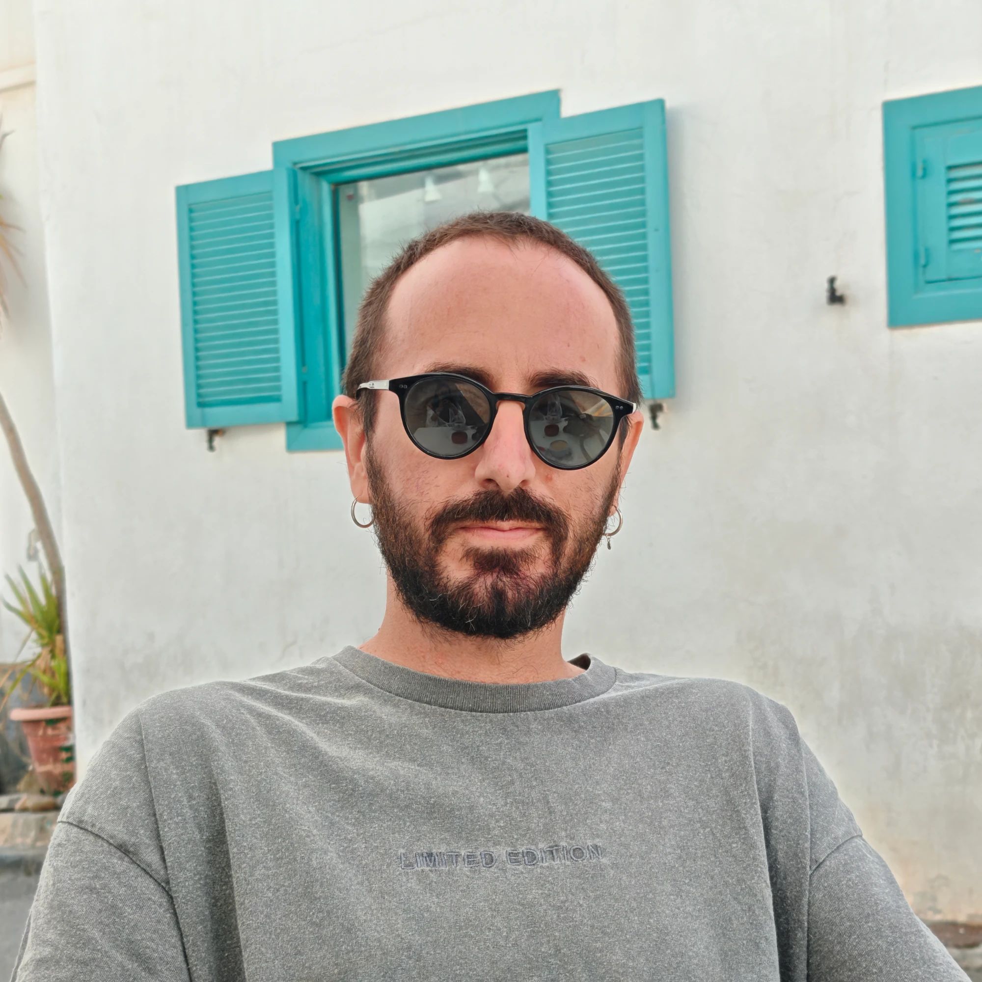 Paco López con gafas de sol delante de una pared blanca con ventanas turquesa